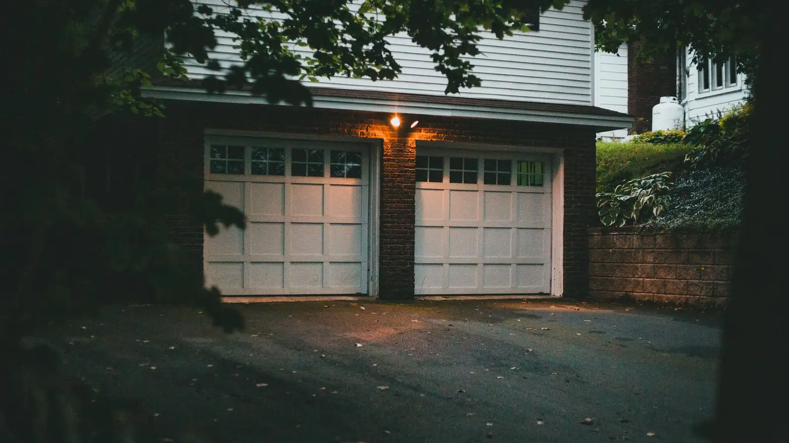 Two white garage doors on a brick-and-siding house at dusk